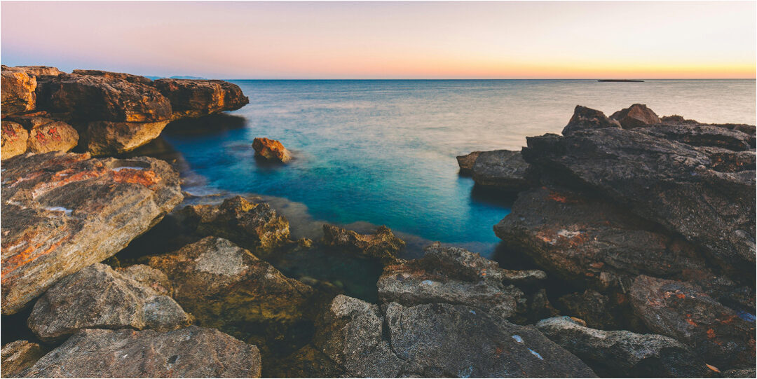 Rocky coastal cliffs and turquoise sea at sunset, tranquil island shoreline view