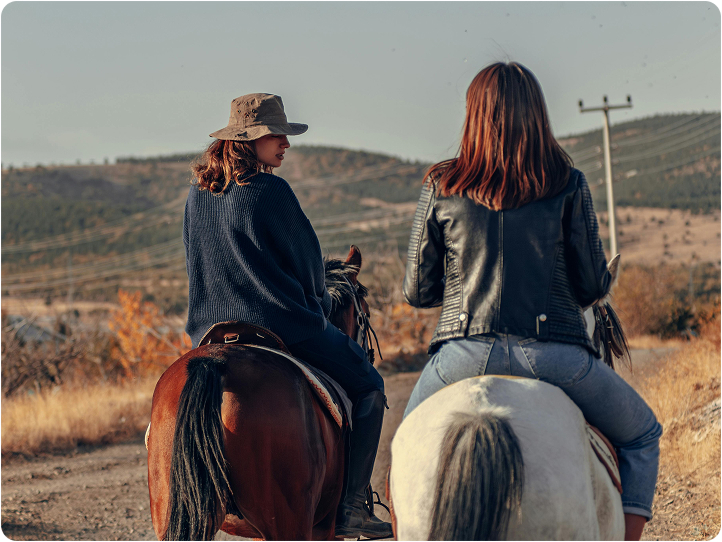 Women horseback riding along a countryside trail with rolling hills in the background