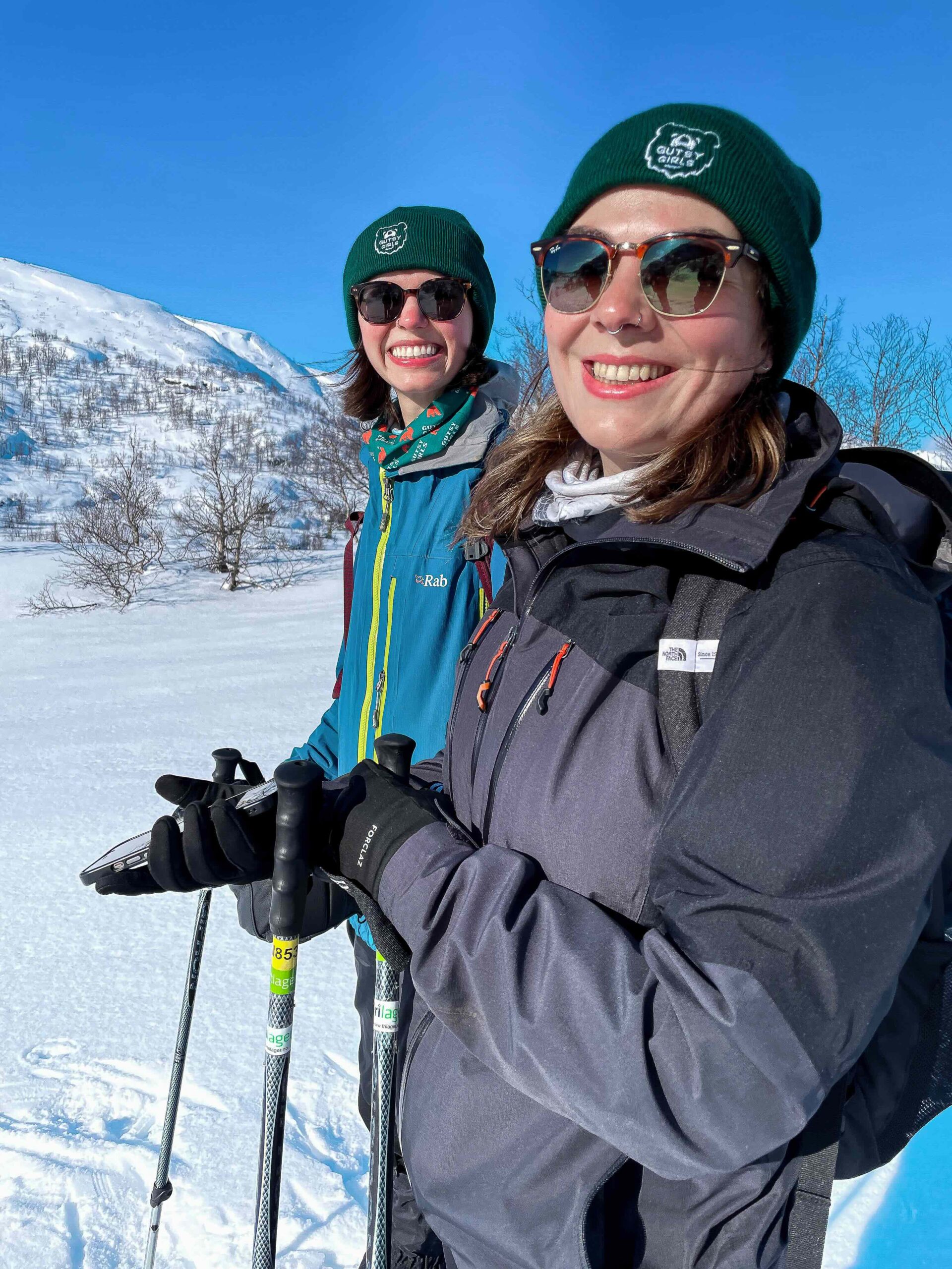 Women skiing on snowy mountains, wearing “Gutsy Girls” hats and holding ski poles outdoors