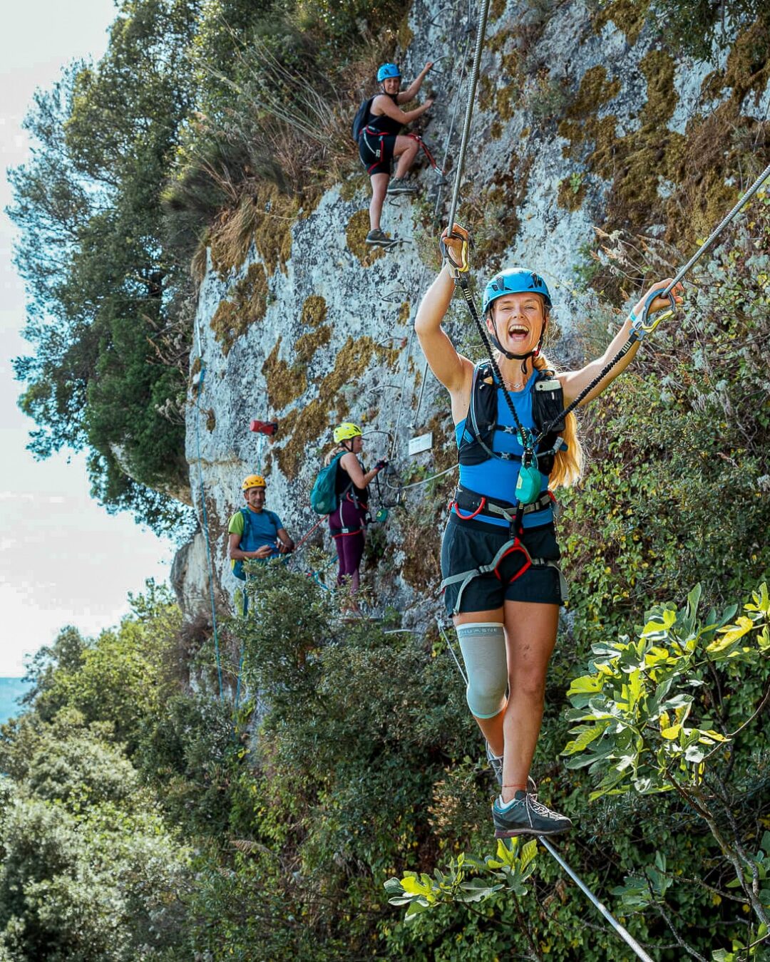 Women rock climbing on a rope on a rocky cliff face, wearing helmets and harnesses outdoors.