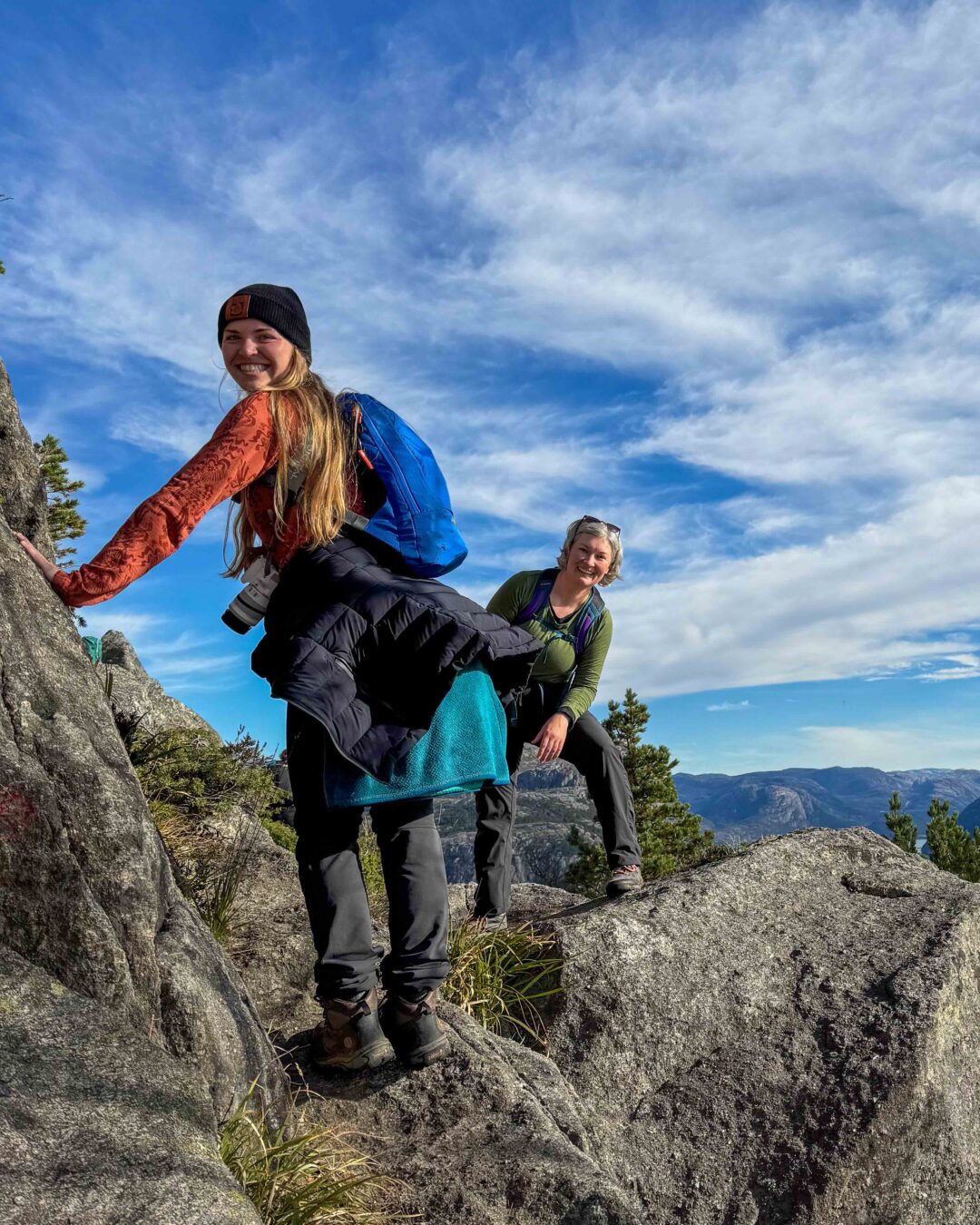 Women hikers in outdoor adventure gear on rocky hilltops, surrounded by mountains and blue sky