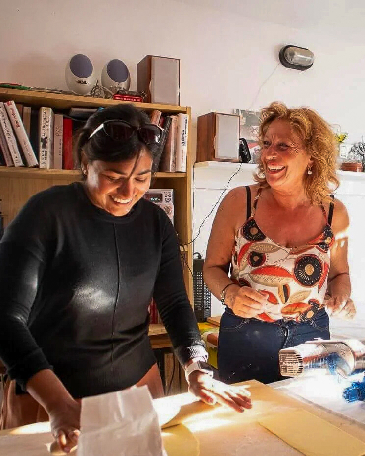 Two women crafting together at a table indoors, smiling while working with materials