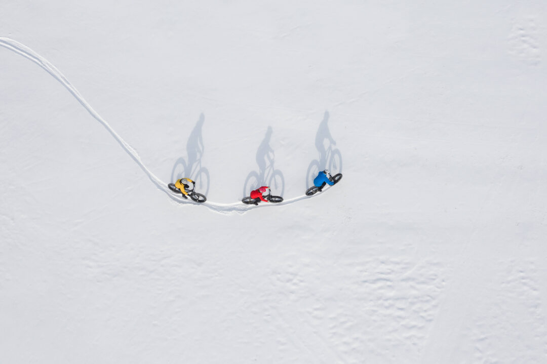 Three snowboarders glide down a snowy slope at a steep ski area