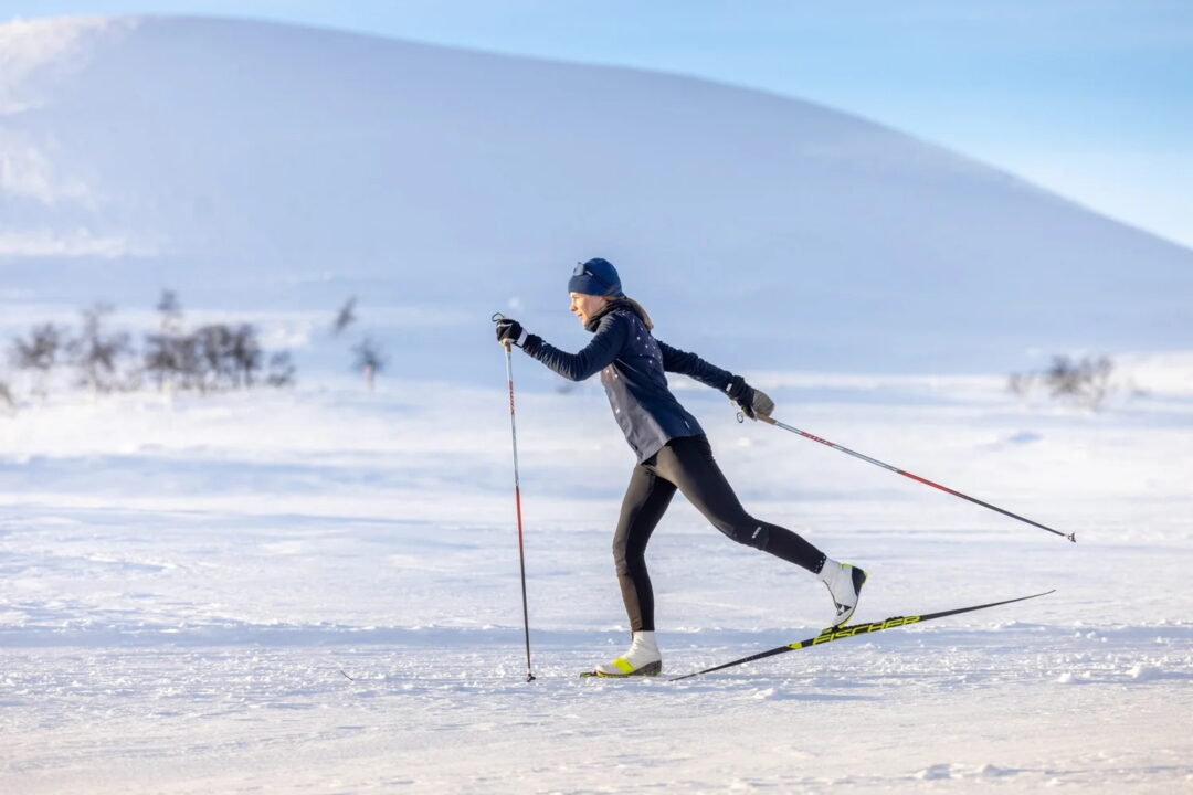 Woman cross-country skiing with poles on a snowy track in a mountain landscape