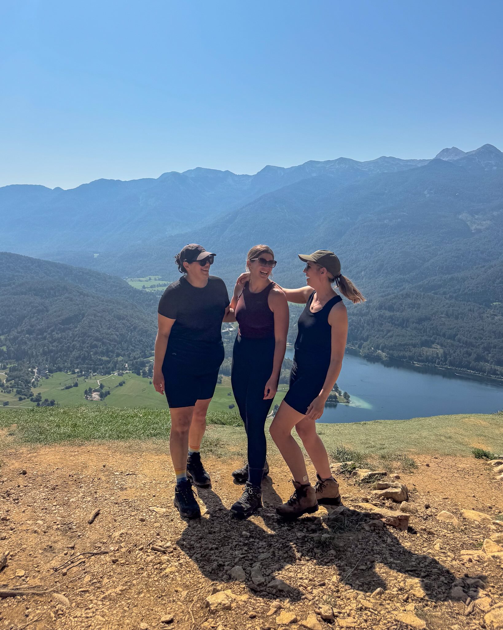 Three women hiking at a mountain viewpoint overlooking a lake and valley with distant peaks