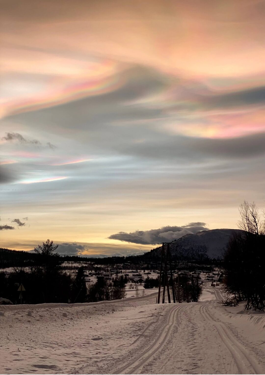Nacreous clouds with a rainbow-like glow over a snowy landscape and winding road at dusk