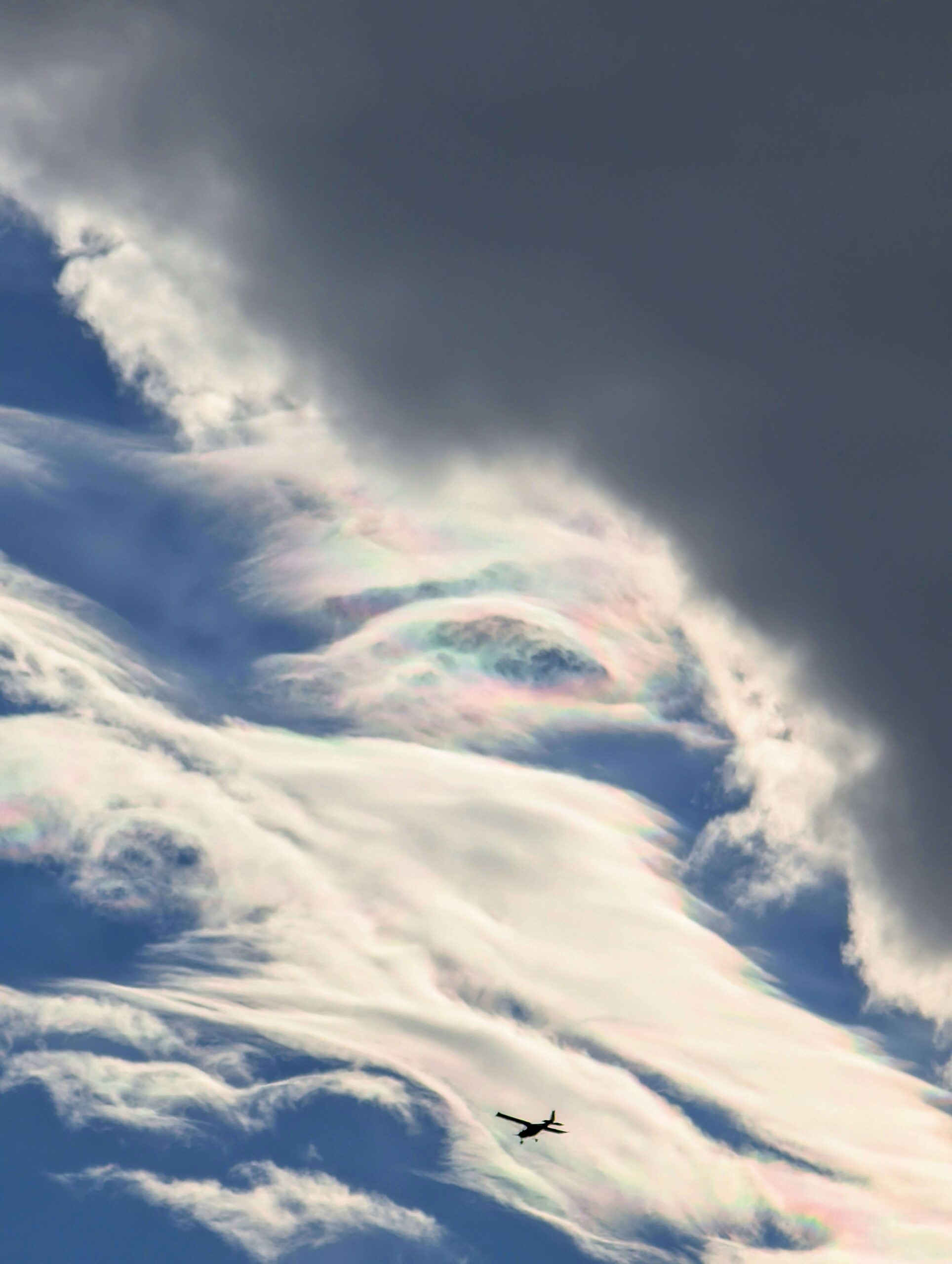 Nacreous clouds with pastel iridescence across the sky and a plane silhouette flying below