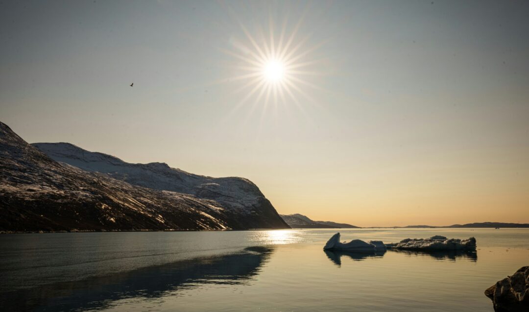 Midnight sun over a calm Arctic fjord with mountains and a moored boat at dusk