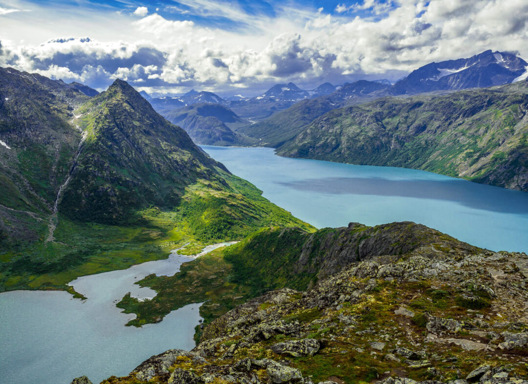 Norwegian fjord and mountain valley panorama with glacial water, rocky slopes and dramatic clouds