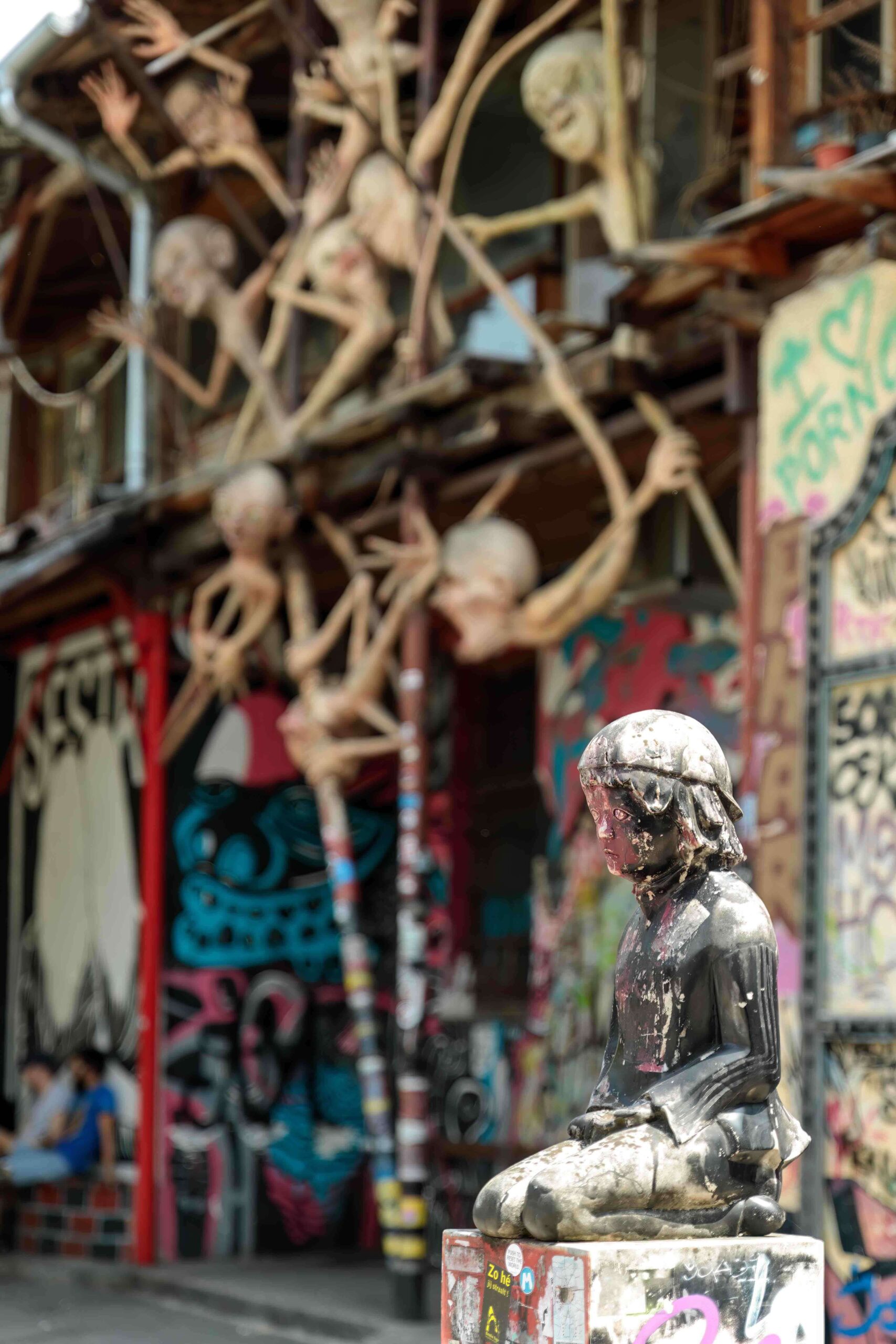 Graffiti-covered courtyard with a painted metal statue in the foreground at Metelkova Mesto, Ljubljana