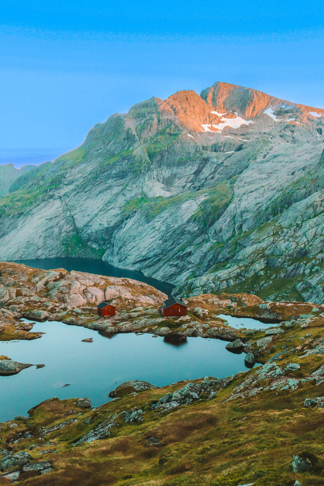 Munkebu hut trail in Norway: two red mountain cabins by a calm lake under steep peaks