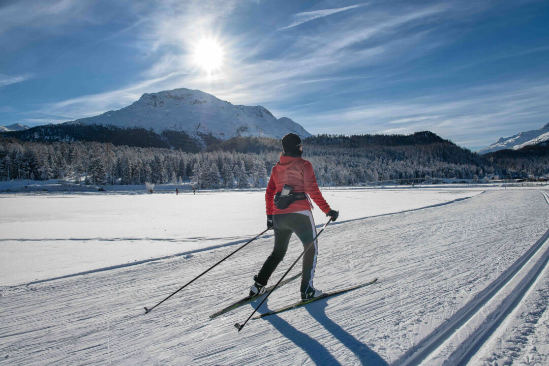 Skate skiing on a snowy track, with mountains and a frozen lake in the background.