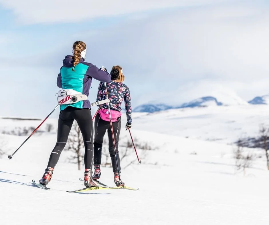Two women skate-skiing on snow with Swix skis, in a mountainous winter landscape