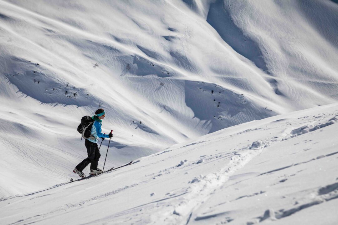 Women ski touring in backcountry on a snowy mountain slope.