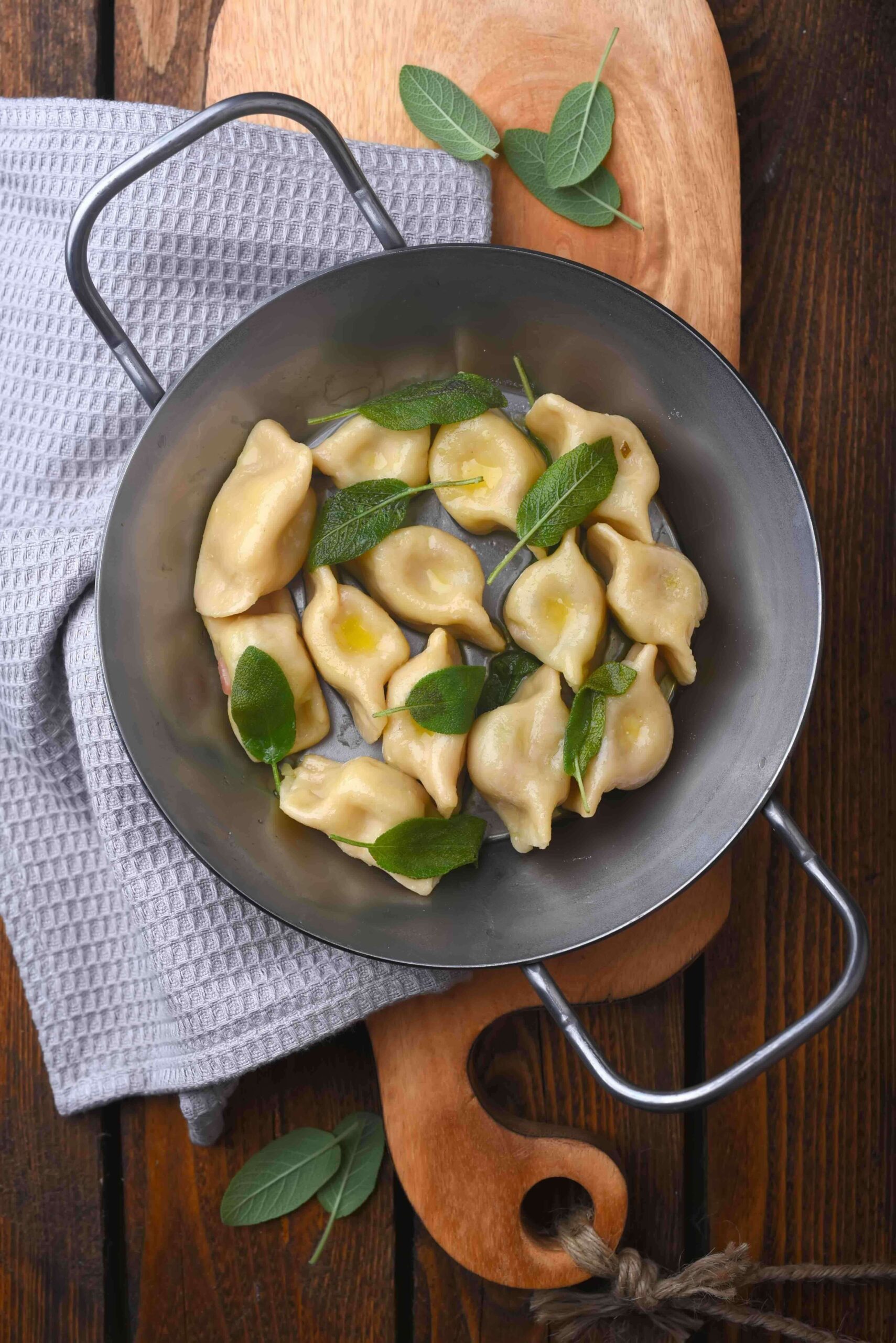 Traditional Slovenian dumplings in a frying pan with fresh sage leaves on a wooden table