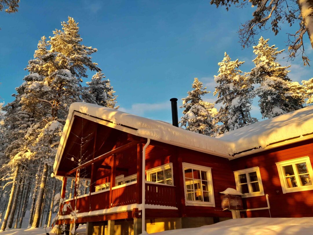 Snow-covered wooden cabin in a winter forest with pine trees under clear blue sky