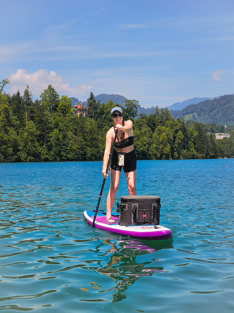 Woman paddleboarding on a lake in Slovenia, calm summer water with mountains and forest in the background