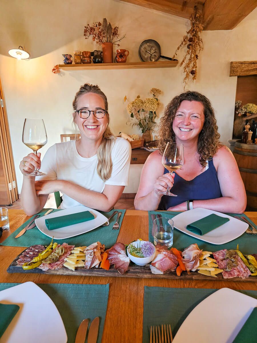 Two women toasting with wine at a table with charcuterie and cheese in a cosy dining room.