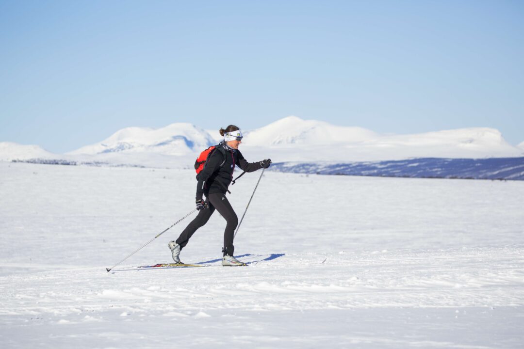 Woman cross-country skiing across snowy landscape with mountains in Sweden