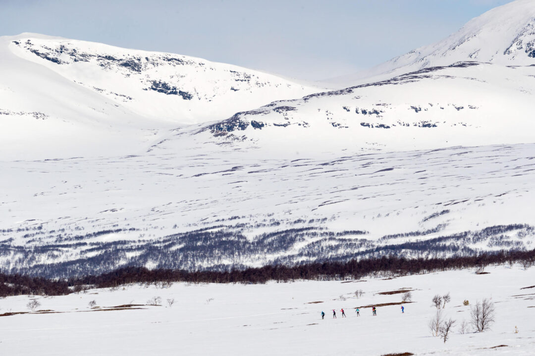 Cross-country skiers travelling across a snow-covered valley between mountain slopes