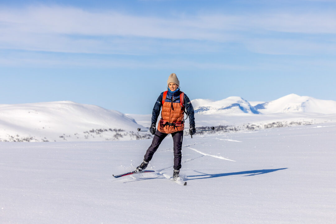 Woman skate skiing on snowy mountains, wearing winter gear and backpack on ski trail