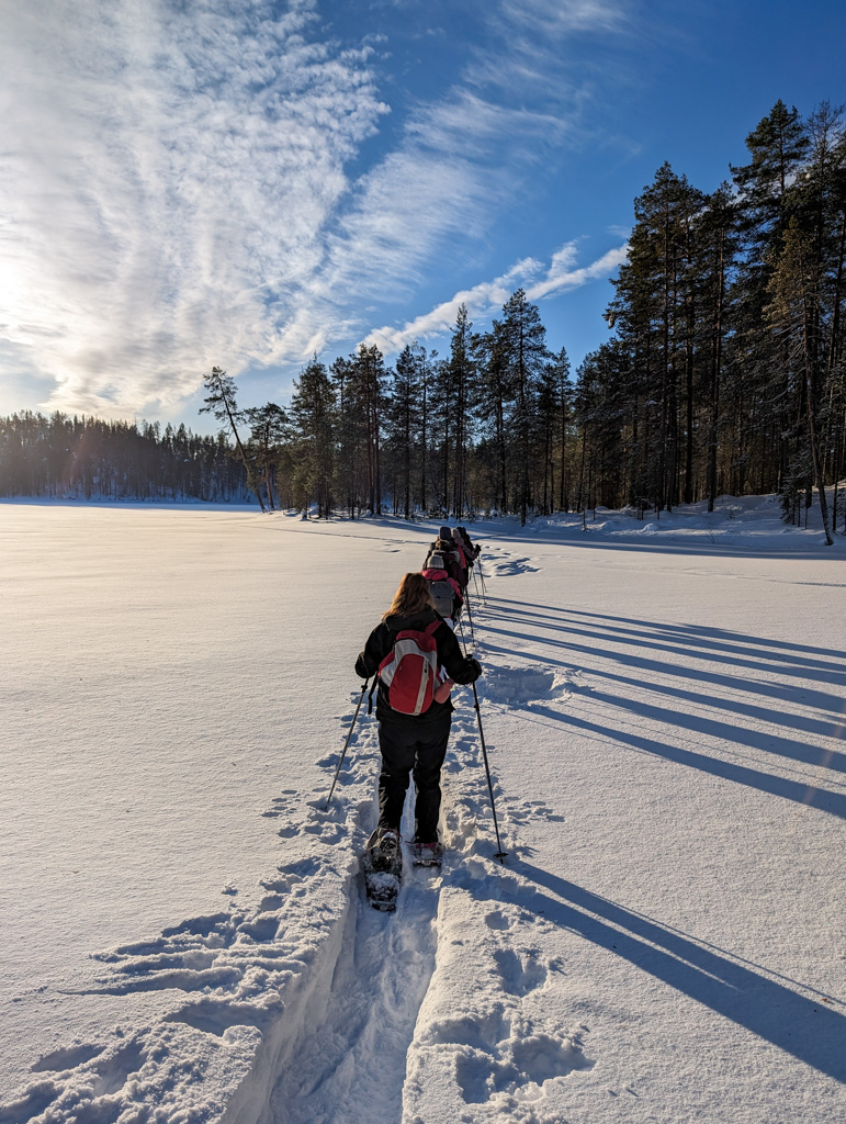 Women snowshoeing across a snowy forest track in Finland under a clear winter sky