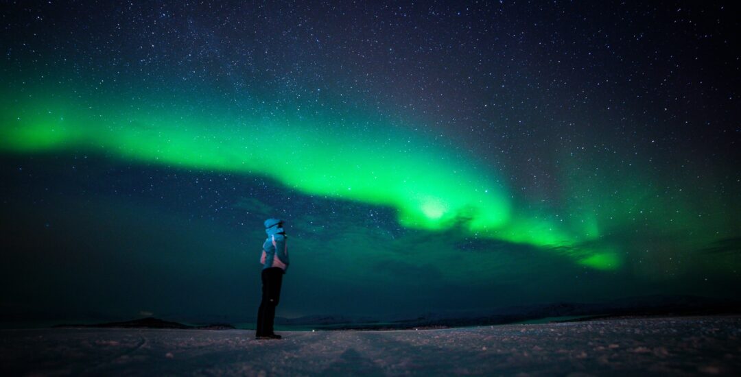 Woman stands on snowy landscape under green aurora borealis in dark night sky