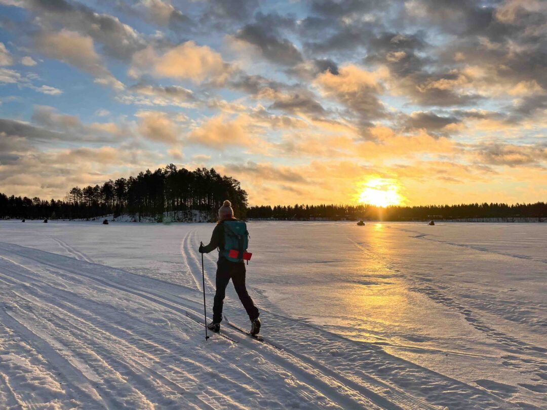 Woman cross-country skiing on a snowy track on a frozen lake at sunset