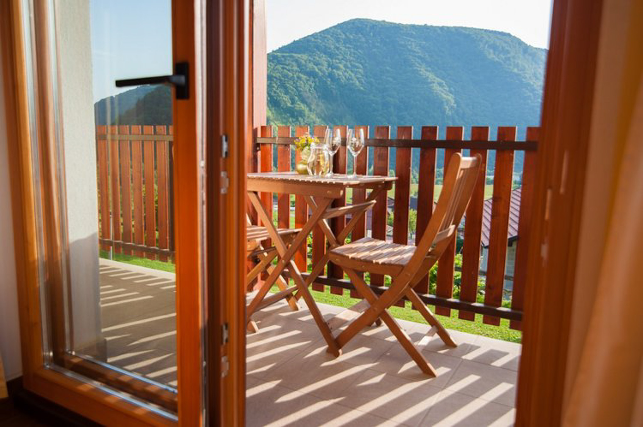Sunlit wooden balcony with table and chairs overlooking mountains in Slovenia