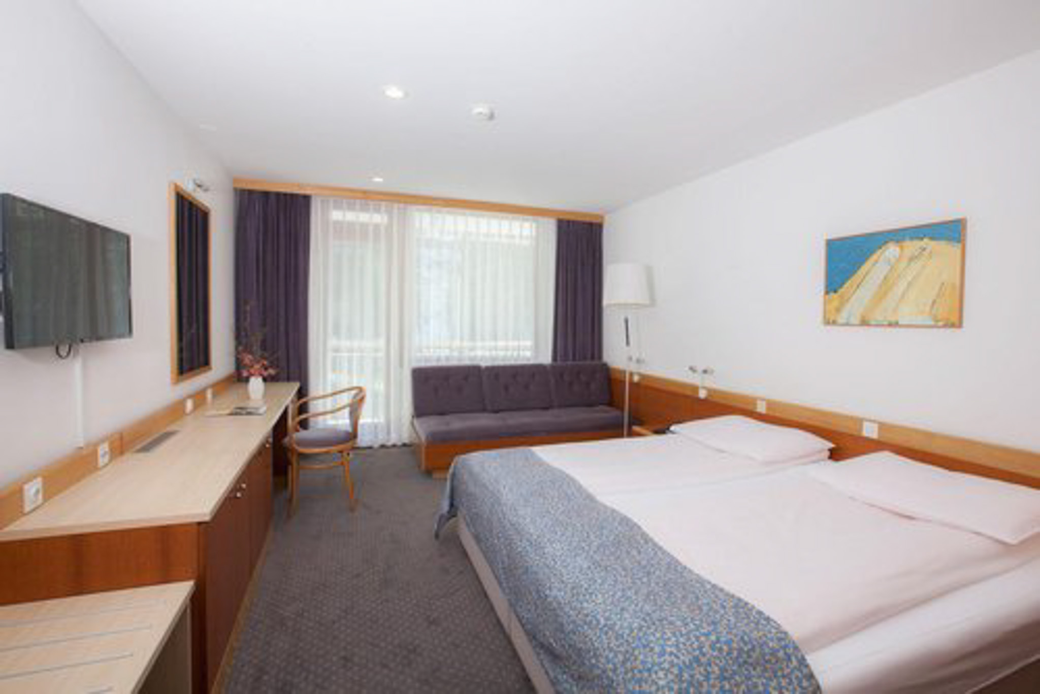 Hotel room interior with twin beds, sofa, desk and lamp in a modern guest suite.