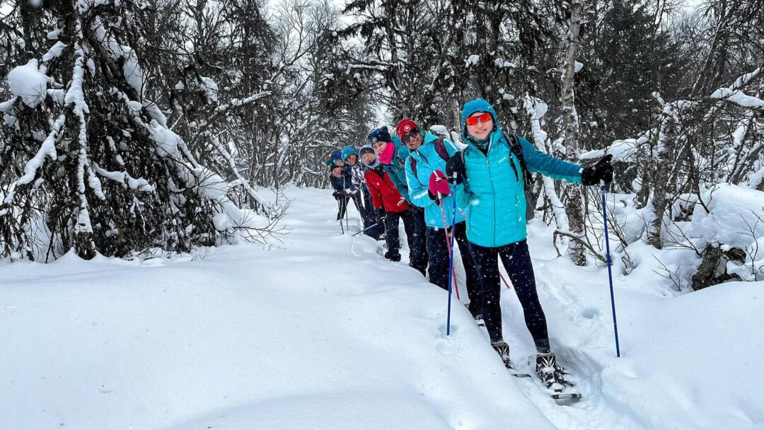 Women snowshoeing on a snowy forest trail with trekking poles, winter adventure outdoors