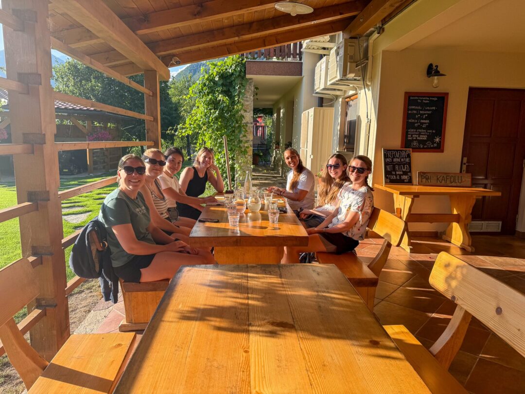 Women enjoying breakfast together at a wooden terrace table in warm sunshine outdoors