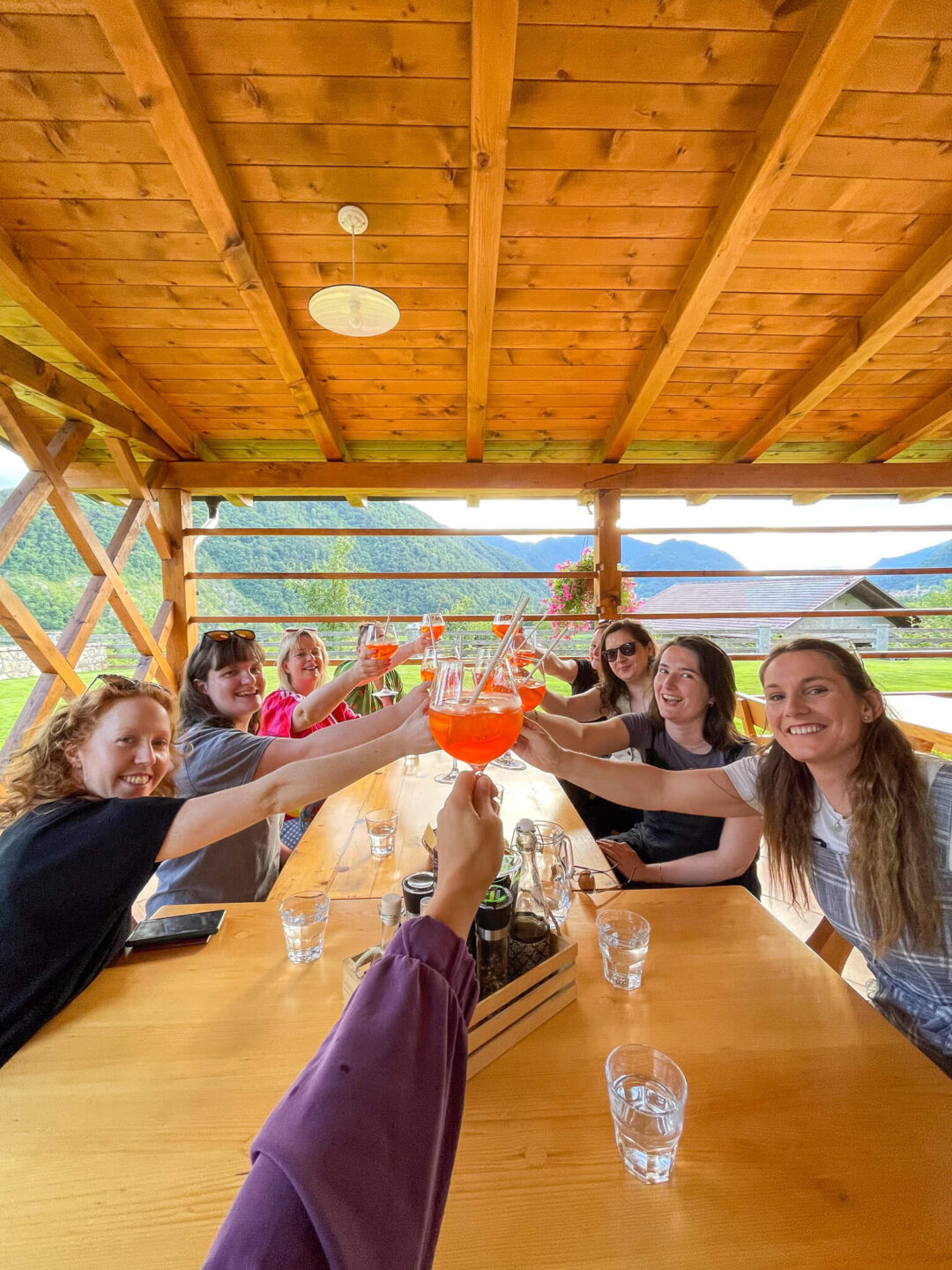 Women friends toasting with orange drinks inside a wooden lodge with mountain views in Slovenia