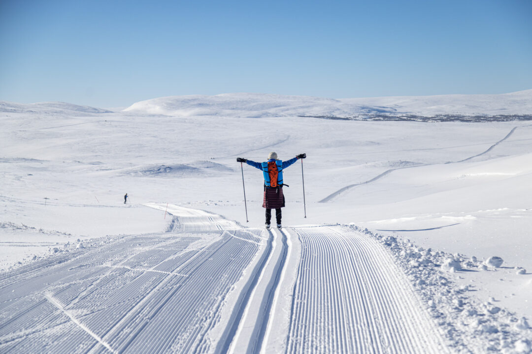 Woman cross-country skiing on snowy trails in Sweden, arms outstretched on a ski route.
