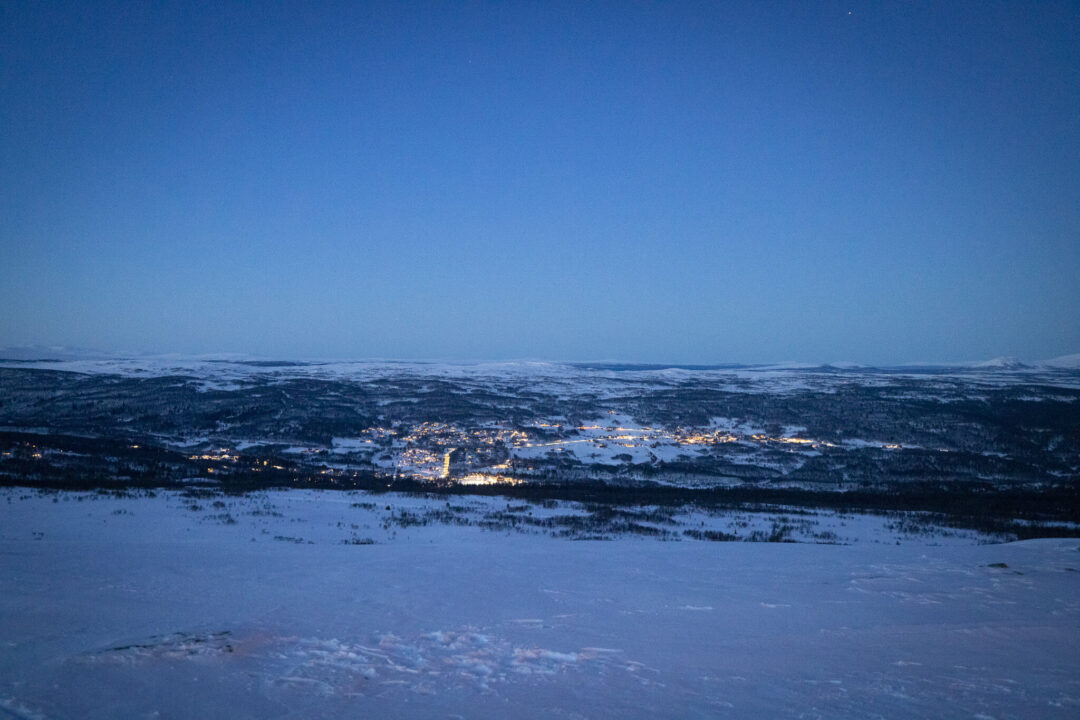 Snowy valley landscape over a Swedish town at dusk, with hills and lit buildings