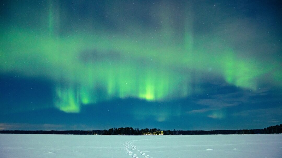 Green northern lights over a frozen lake and snowy landscape at night