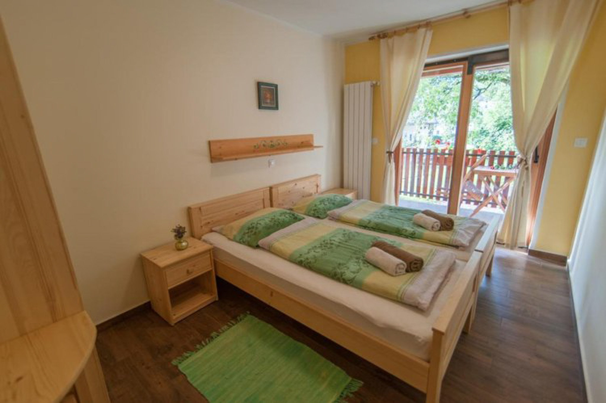 Bedroom with double bed and green bedspread, wooden headboard, and a door to a balcony with railings.