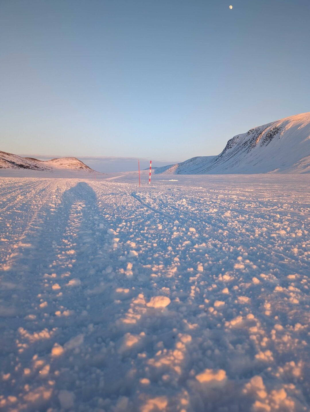 Snowy Arctic landscape with red-and-white ski poles on an icy track at dusk