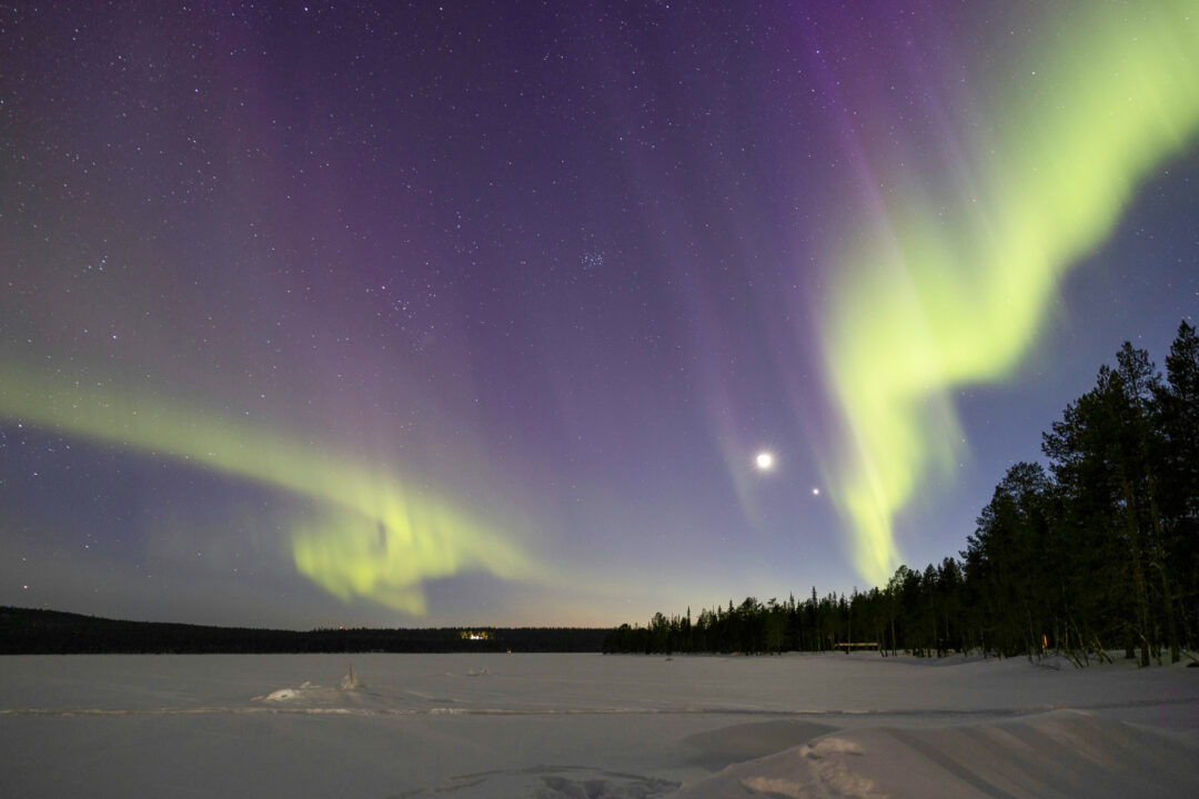 Northern lights over snowy landscape with forest and lake in Finland at night