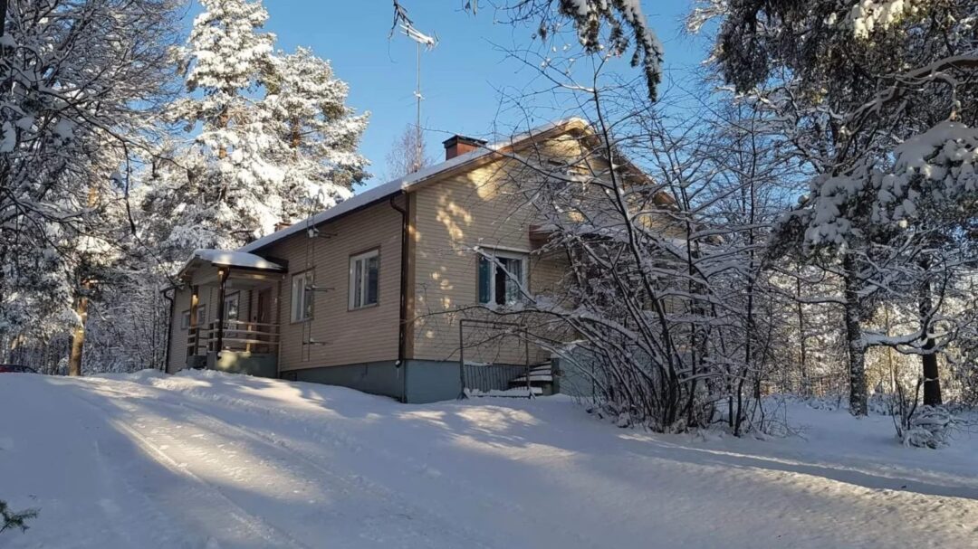 Snow-covered wooden cabin in a Finnish winter forest, with trees dusted in snow and blue sky
