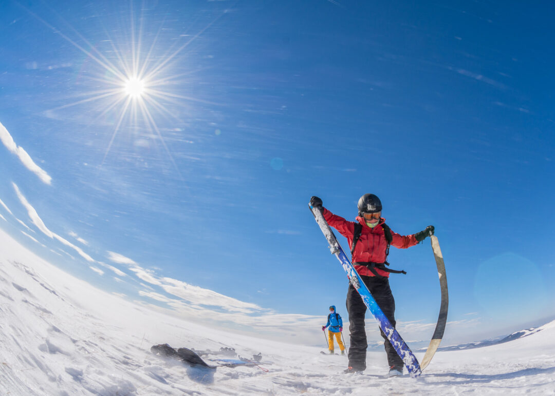 Skier trekking uphill on skis across snowy slopes under bright sun in the mountains