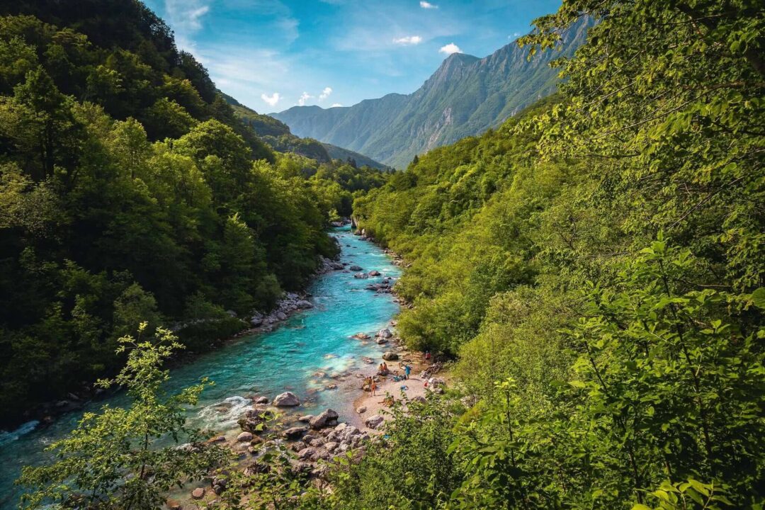 Scenic Slovenian river valley with hikers along turquoise water and forested mountains