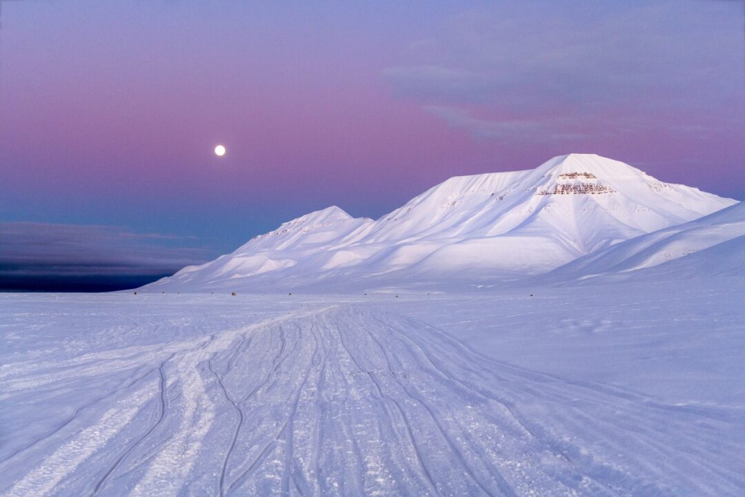 Snowy mountains at night under a purple twilight sky with a bright moon, Arctic winter landscape