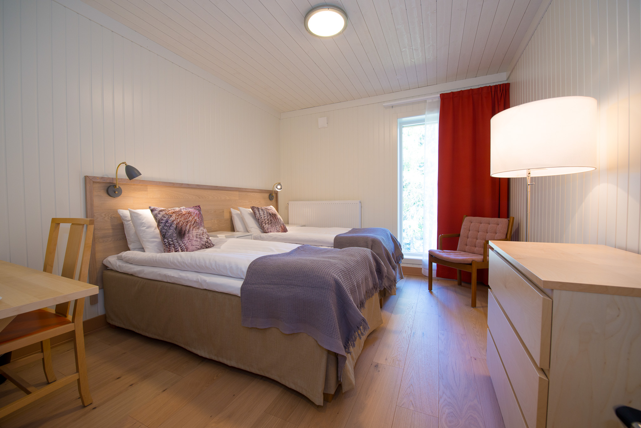 Hotel room with two beds, red curtains, bedside lamps and a window