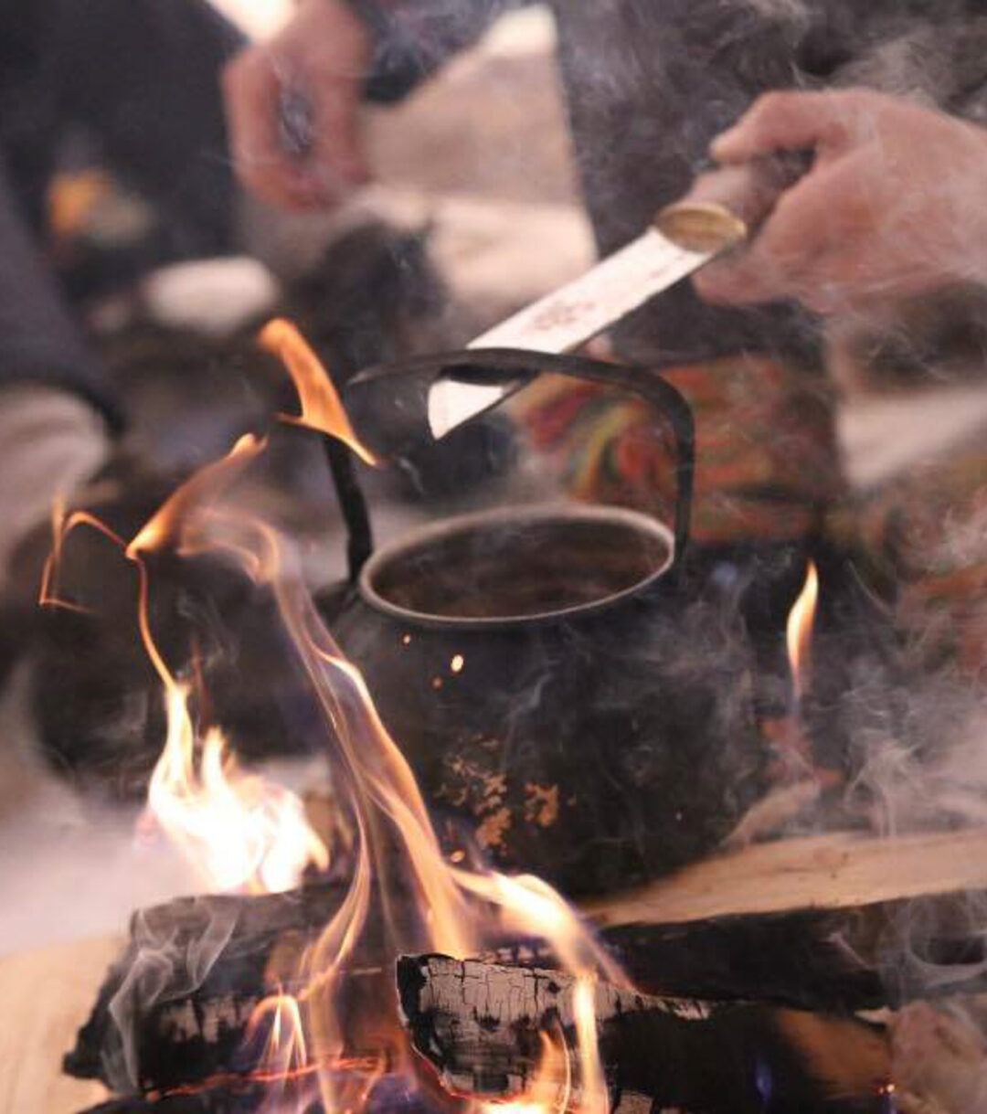 Open campfire in Lapland with a kettle boiling as people cook by the winter flames outdoors