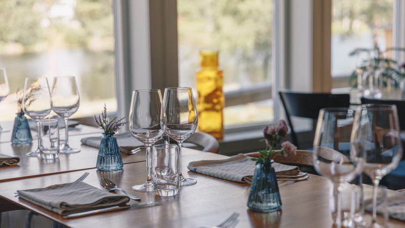 Neatly set dining table with stemware and blue glass vases by large windows in Swedish Lapland lodge