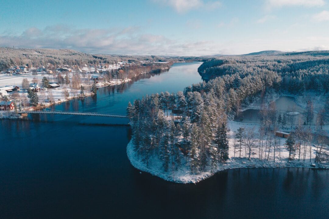 Aerial winter landscape of a snowy forest village by a calm river in Lapland