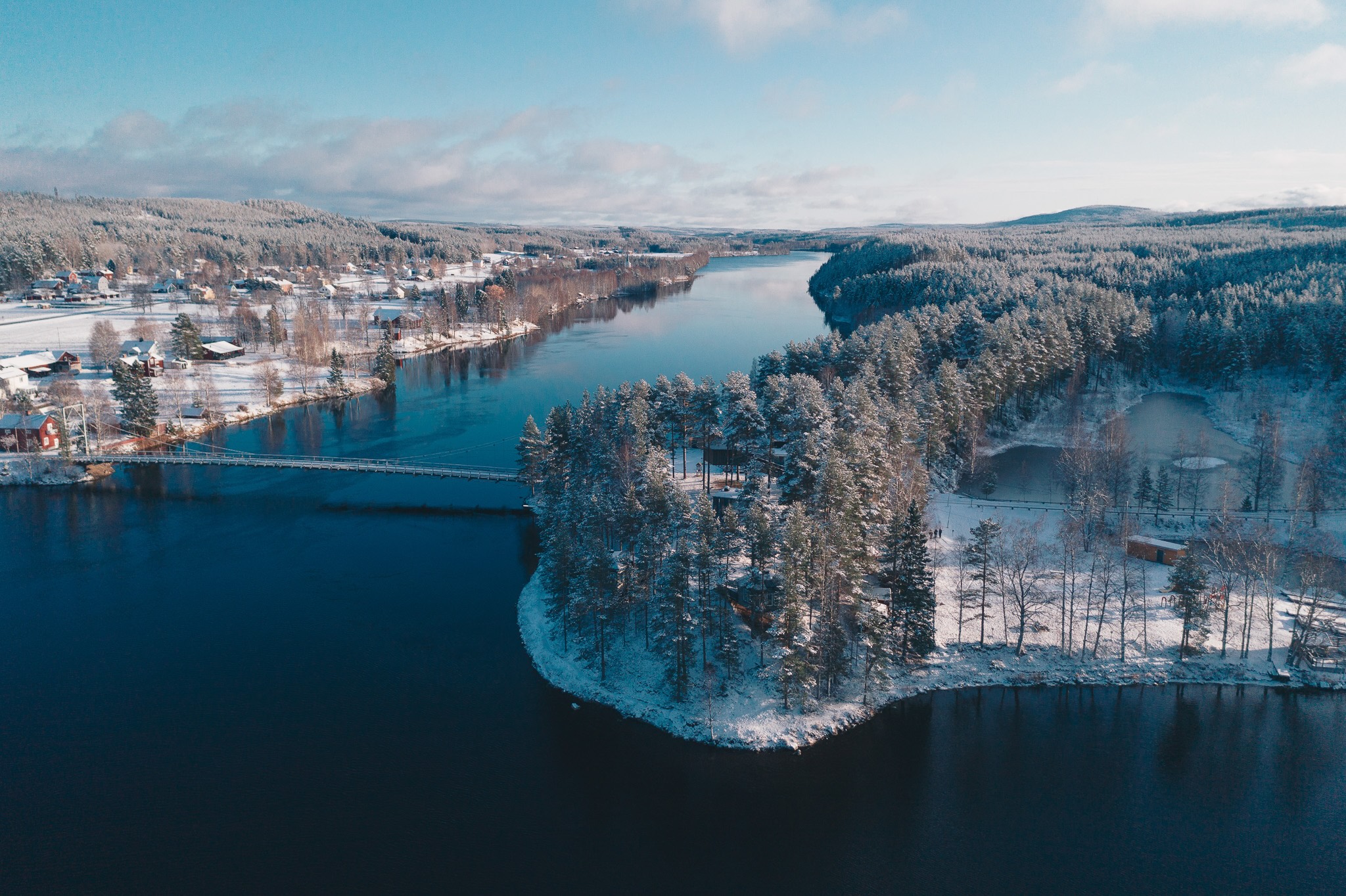 Aerial winter landscape of a snowy forest village by a calm river in Lapland