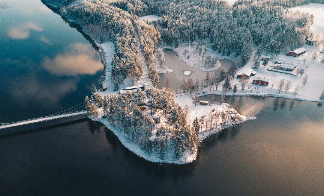Aerial view over a snowy Swedish Lapland lake and forest with cabins along a frozen shoreline