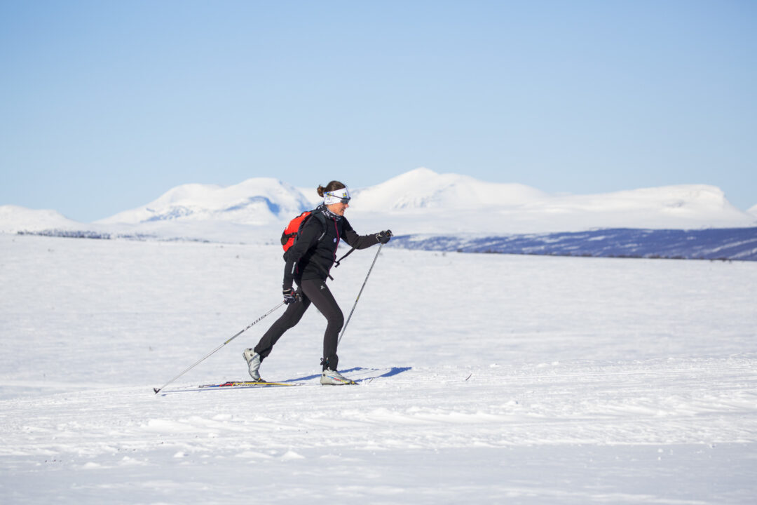 Cross-country skier practising on snowy Sweden landscape with distant mountains under clear sky